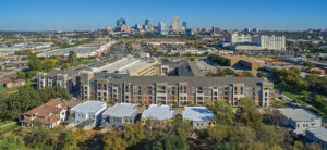 Aerial view of a large brown and white apartment complex with red brick and views of downtown Fort Worth