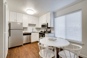Interior view a kitchen area with white cabinets, stainless steel appliances, and and a white table with four chairs