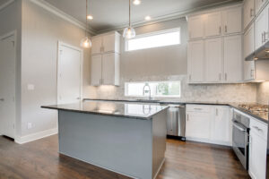 Interior view of a kitchen with white cabinets, white tile backsplash, stainless steel appliances, and a center island