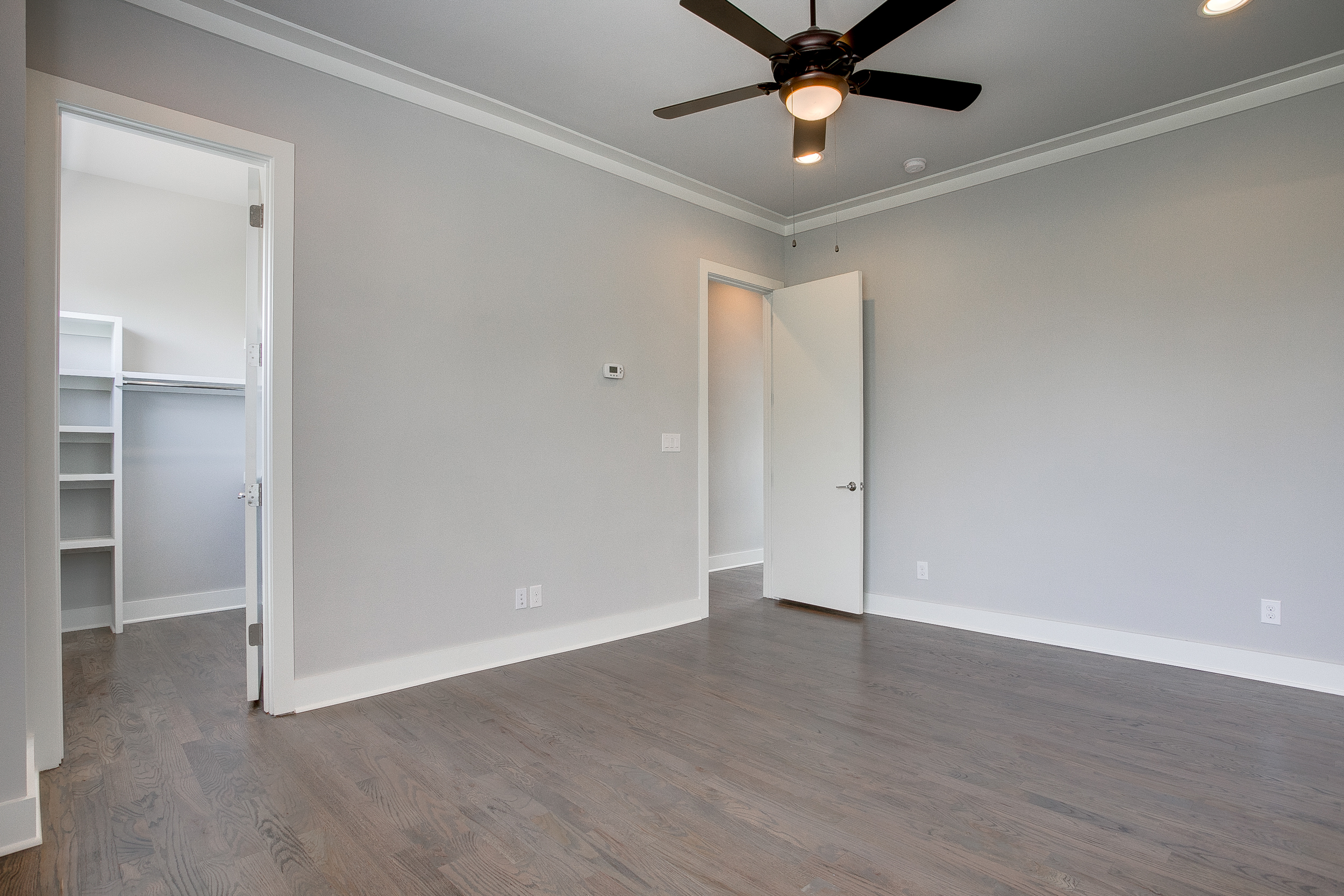 Interior view of an empty bedroom with dark hardwood floors, a ceiling fan, and a view into the walk-in closet