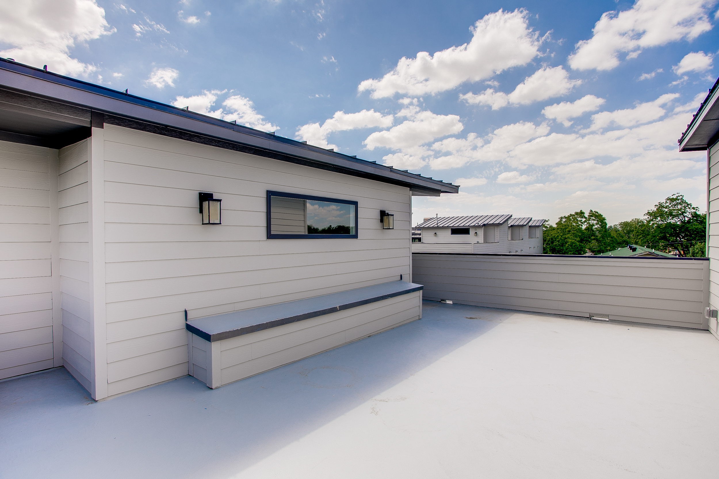 Exterior view of the rooftop deck of the townhome with white siding, a black roof, and views of the surrounding area