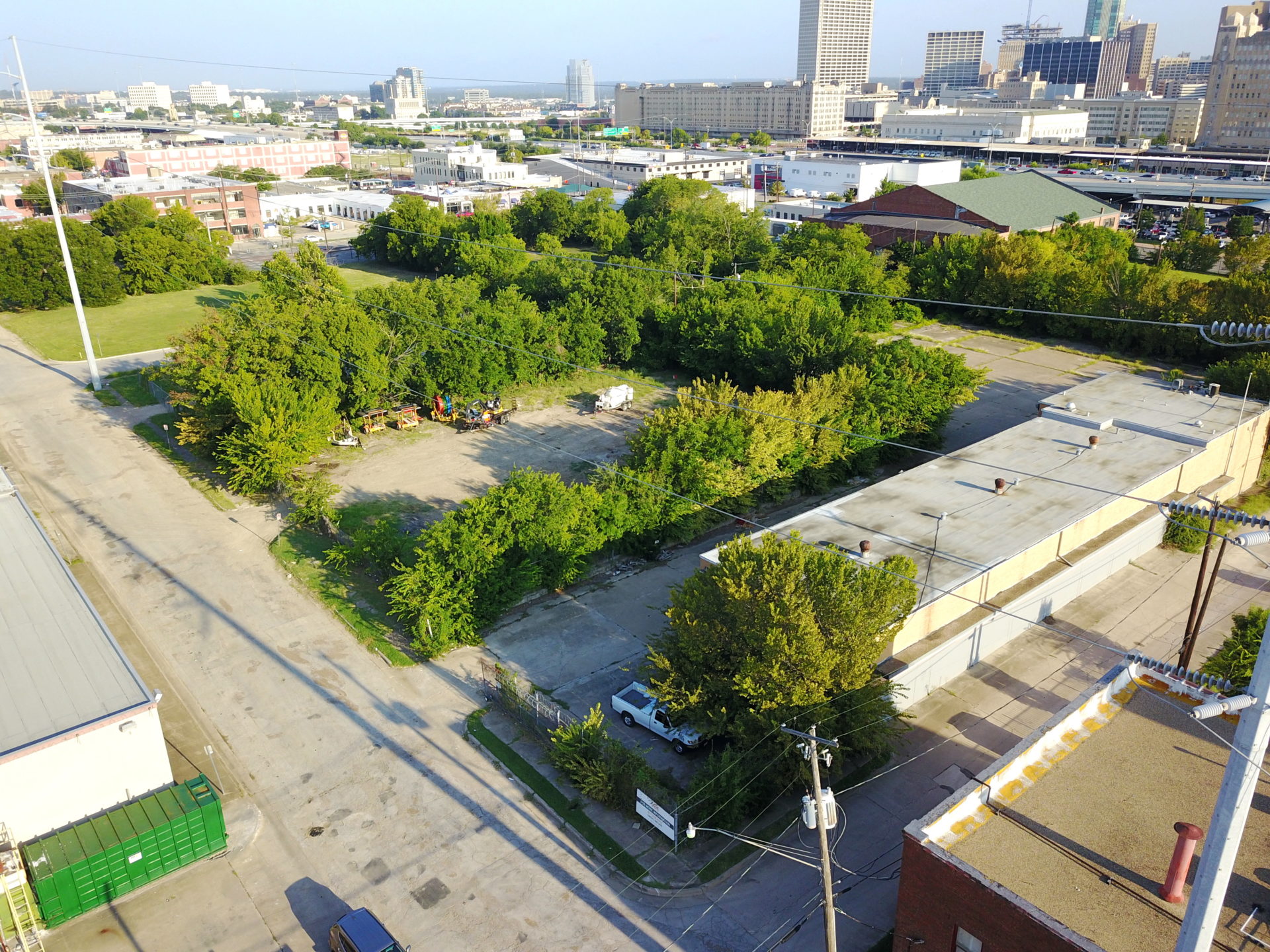 Aerial view of a building with a brown roof, surrounded by multiple green trees, power lines, and an adjacent street