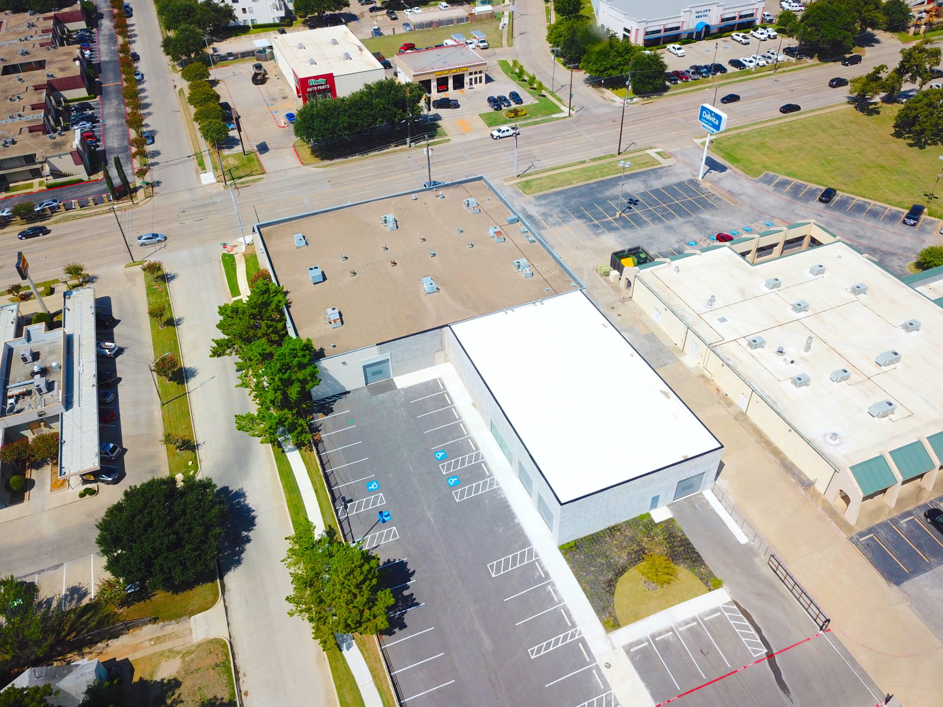 Aerial view of an L-shaped building with a white and brown roof with parking spaces next to the adjacent street