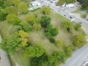 Birds-eye view of a grassy, square plot of land with numerous light and dark green trees throughout the land
