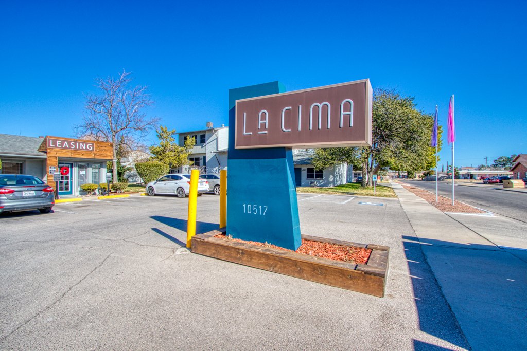 Exterior view of a blue vertical post with a horizontal sign with white lettering saying "La Cima" in a parking lot