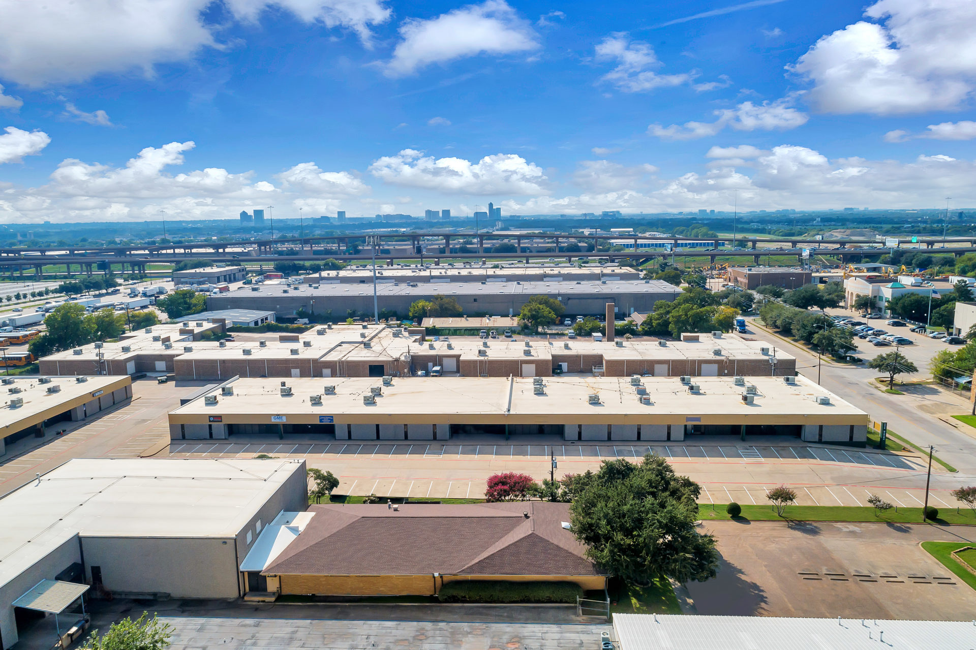 Aerial view of multiple large, warehouse buildings with parking spaces in front and views of the city in the background