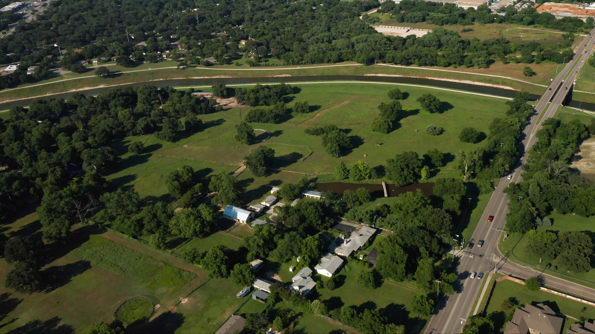 Aerial view of a green farm next to the Trinity River with multiple white houses next to an adjacent road