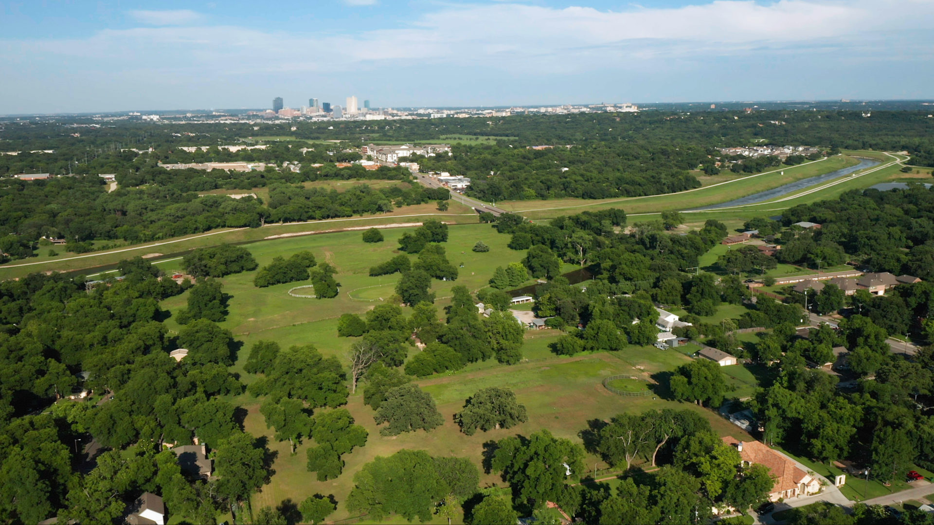 Zoomed out aerial view of a large farm with numerous trees and a view of the Trinity River and downtown Fort Worth