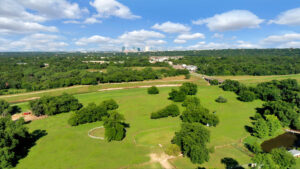 Aerial view of a green farm with multiple trees adjacent to a river and road with a view of downtown Fort Worth