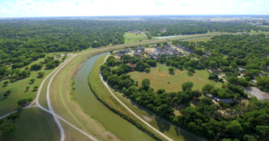 Aerial view of the horseshoe bend of the Trinity River surrounded by numerous green trees and houses in the background
