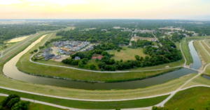 Aerial view of the horseshoe bend of the Trinity River with numerous green trees and developments in the background